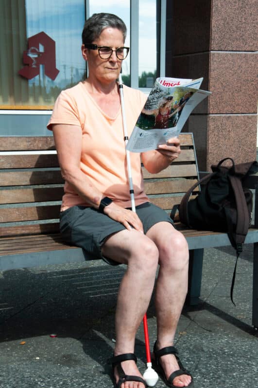 Person reading outdoors on a bench while using the OrCam MyEye